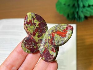 Colorful polished crystal butterfly carvings resting on a palm against a blurred green background