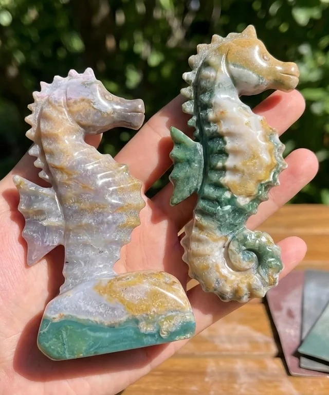 Two polished green and pale stone seahorses held above an outdoor workbench