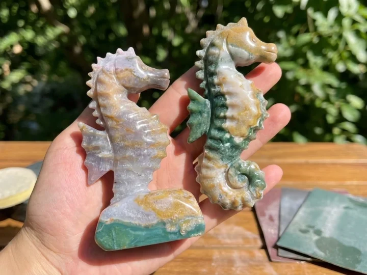 Two polished green and pale stone seahorses held above an outdoor workbench