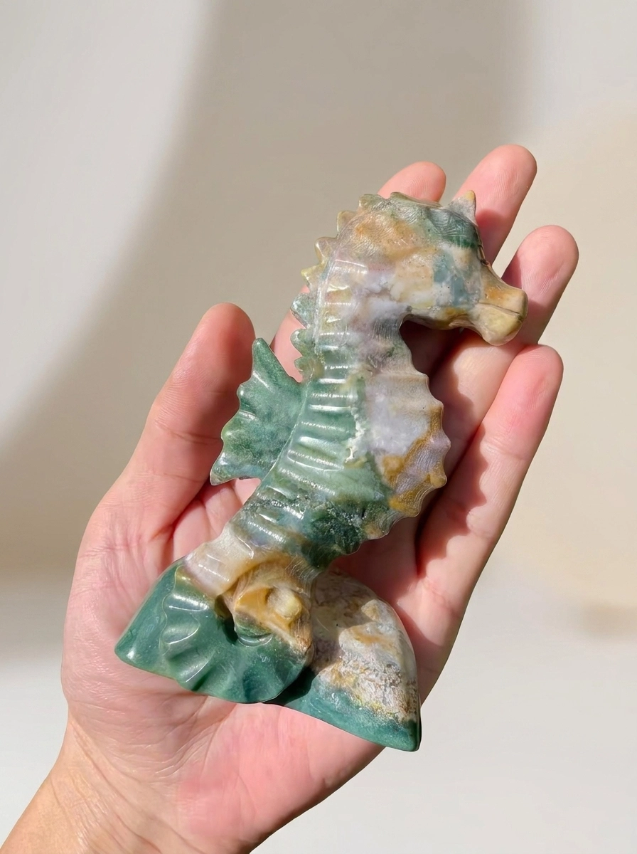 A glossy green, cream, and ochre stone seahorse resting on an open palm
