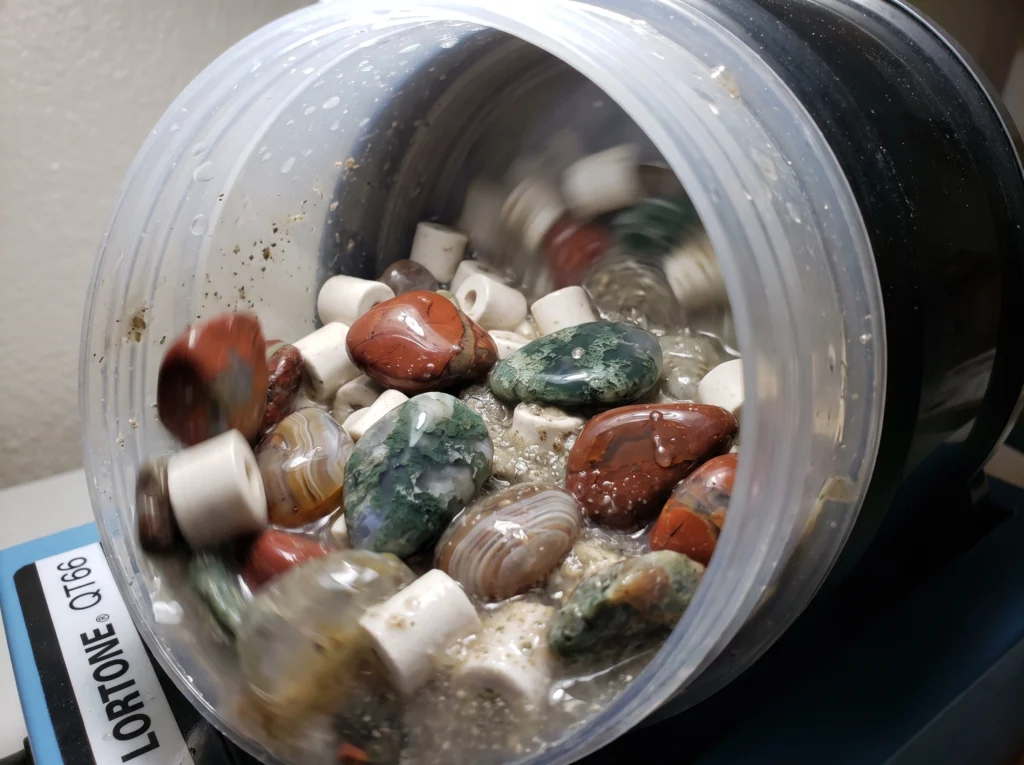 Macro shot of colorful jasper and agate semi-precious stones with ceramic tumbling media inside a rotary rock tumbler barrel.
