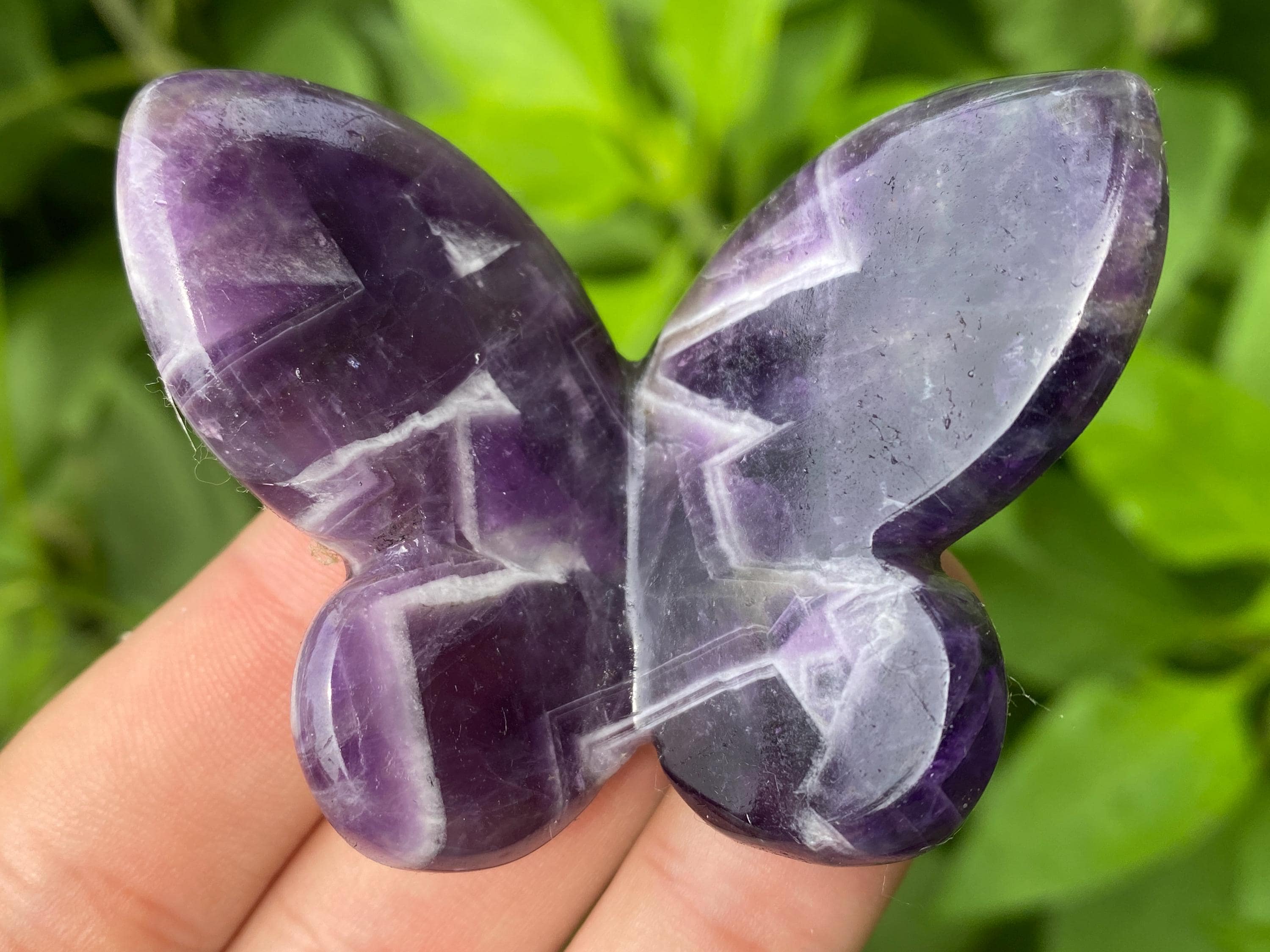 Colorful polished crystal butterfly carvings resting on a palm against a blurred green background
