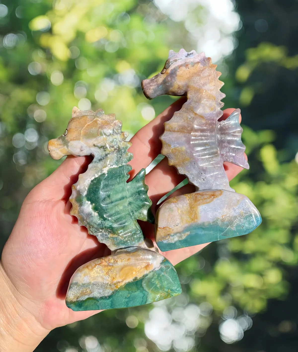 Two ocean jasper seahorse carvings with green and pale mottled patterns held in a palm